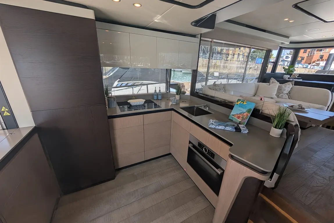 Modern yacht interior featuring a sleek kitchen with an oven, sink, and stylish decor, overlooking a marina.